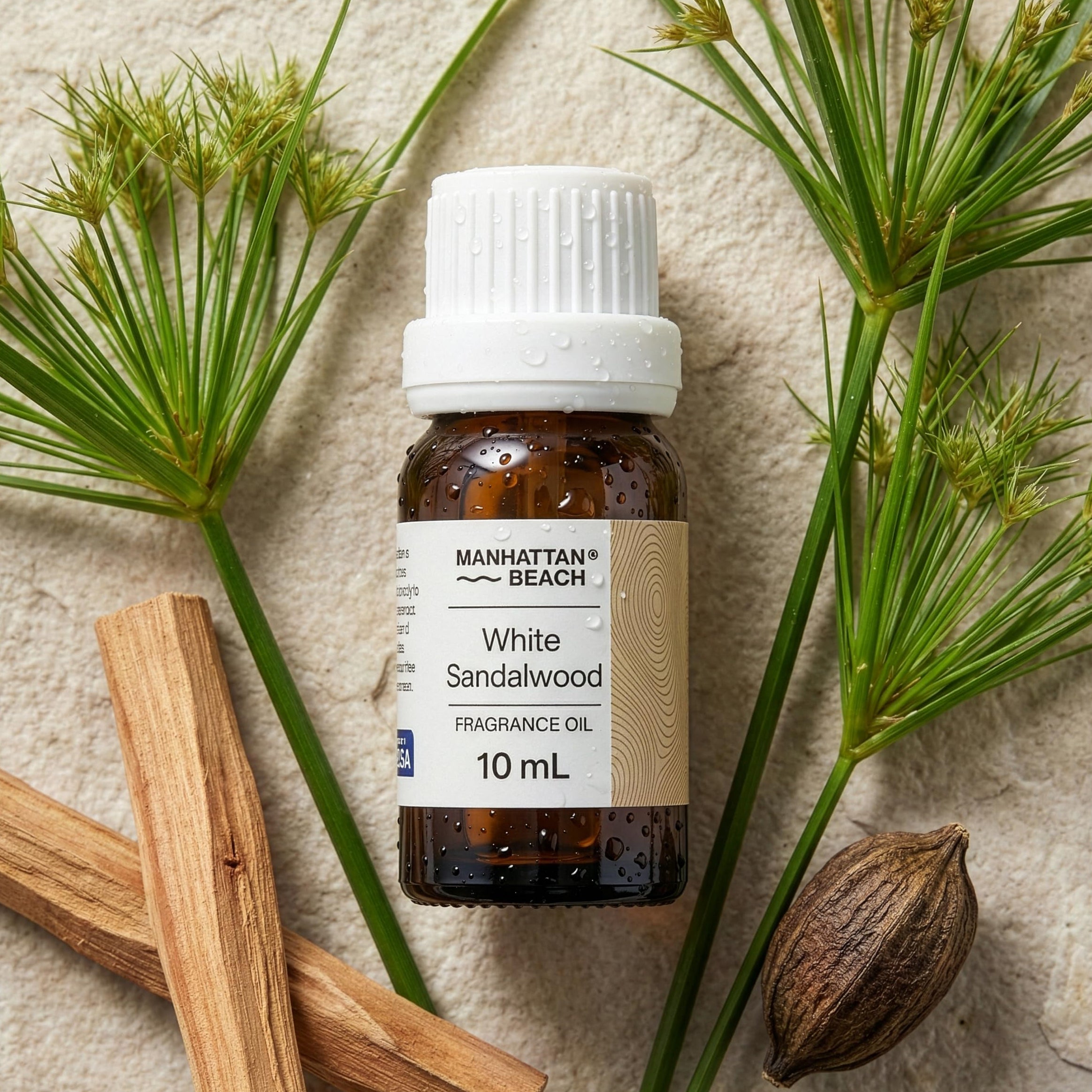 Bottle of Manhattan Beach White Sandalwood fragrance oil with sandalwood and green leaves on a textured surface