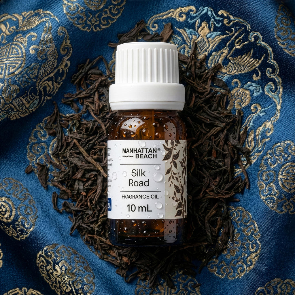 Bottle of Manhattan Beach Silk Road fragrance oil surrounded by dried black tea leaves on a blue patterned silk fabric